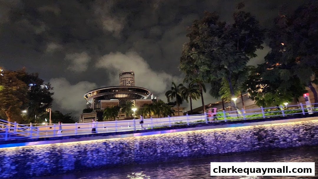 Night view of a riverfront promenade with illuminated buildings and trees.