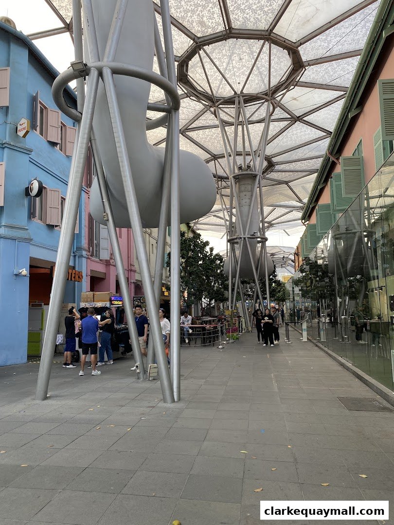 People walking along a covered walkway with colorful buildings and unique architectural structures.