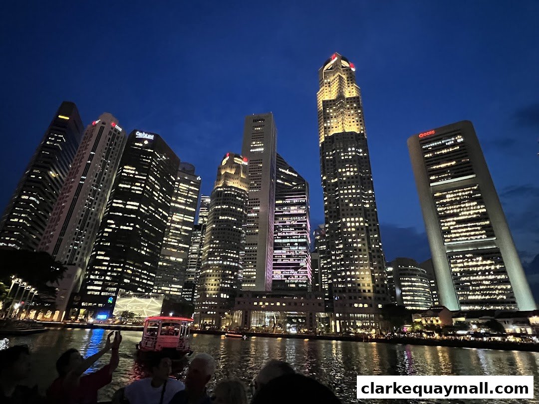 Night view of Singapore skyline with illuminated skyscrapers and a river cruise boat.