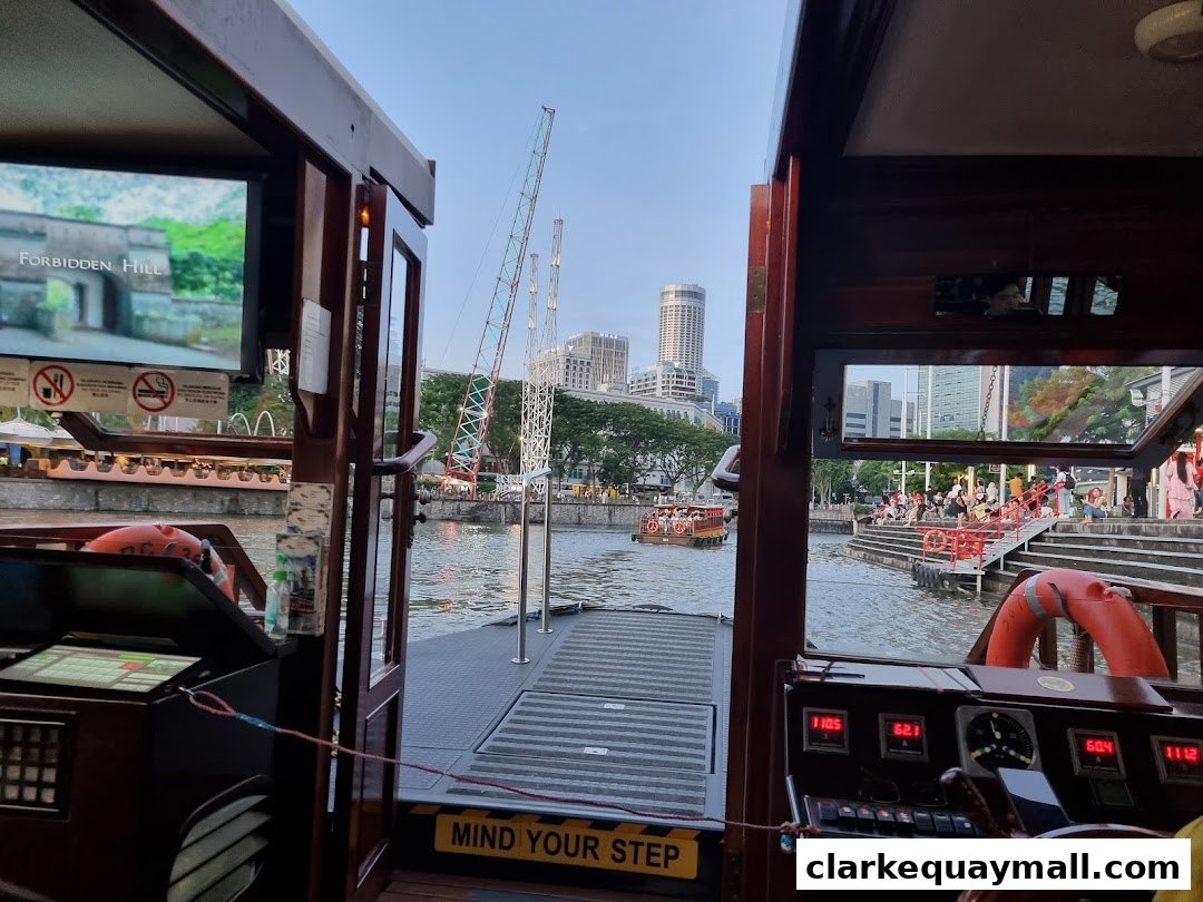 View from a boat's cabin showing a river cruise with city skyline and people on the banks.