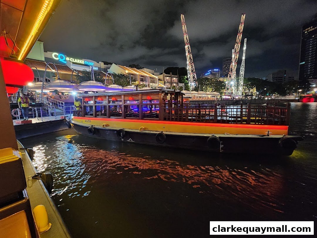 A boat docked at Clarke Quay at night, with illuminated buildings and towers in the background.