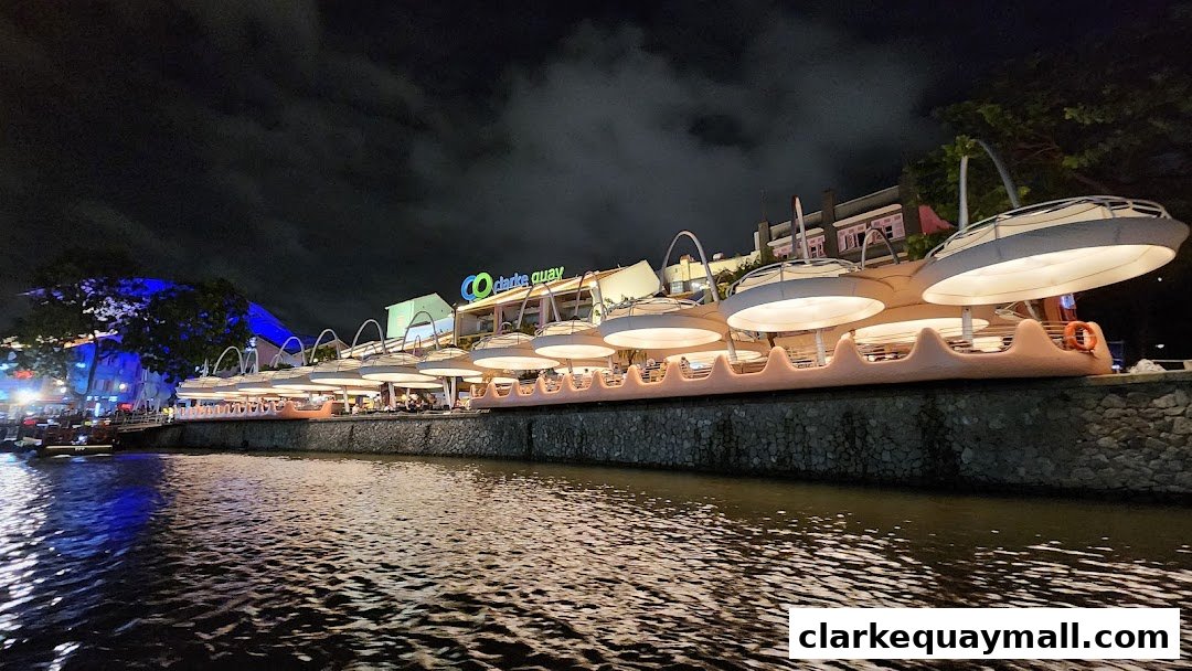 A waterfront view of illuminated shops and restaurants at Clarke Quay at night.