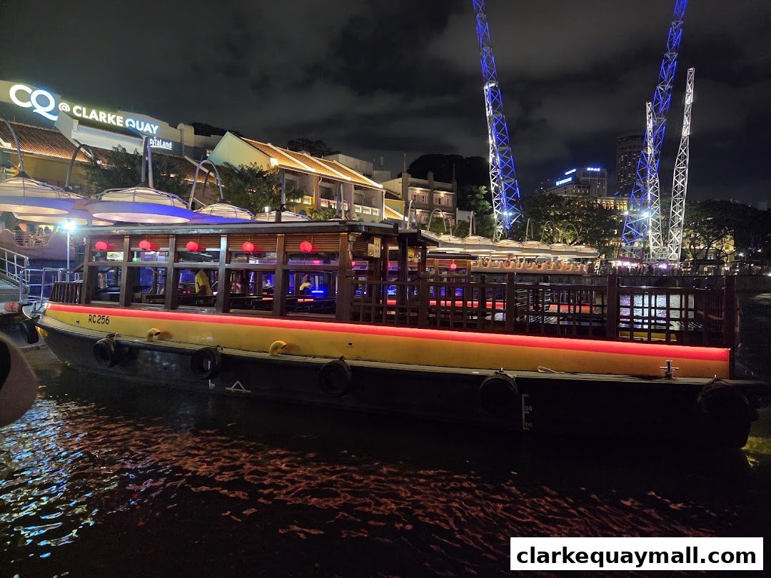 A boat restaurant at Clarke Quay at night, with illuminated towers in the background.