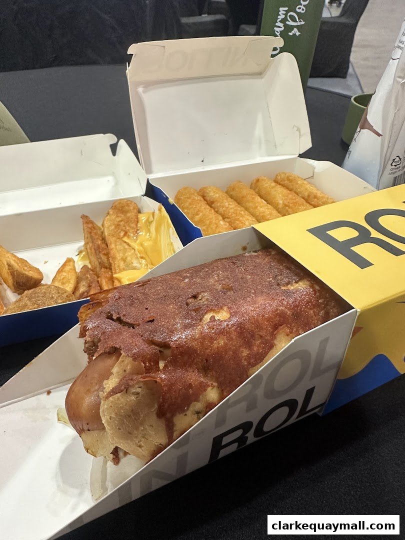 A close-up of a cheese-covered hot dog and sides of potato wedges and hash browns.