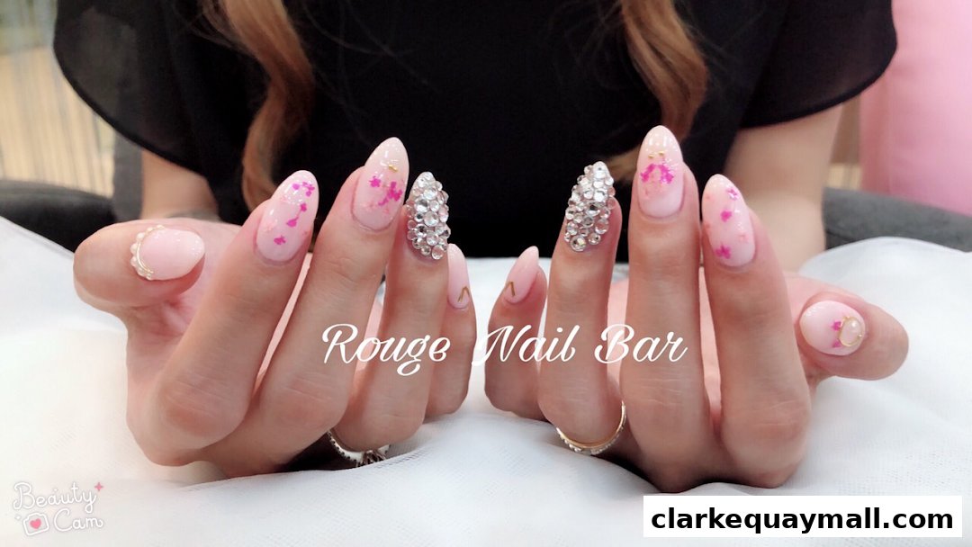 Close-up of hands with elaborate pink and crystal-embellished nails, featuring the shop name 'Rouge Nail Bar'.