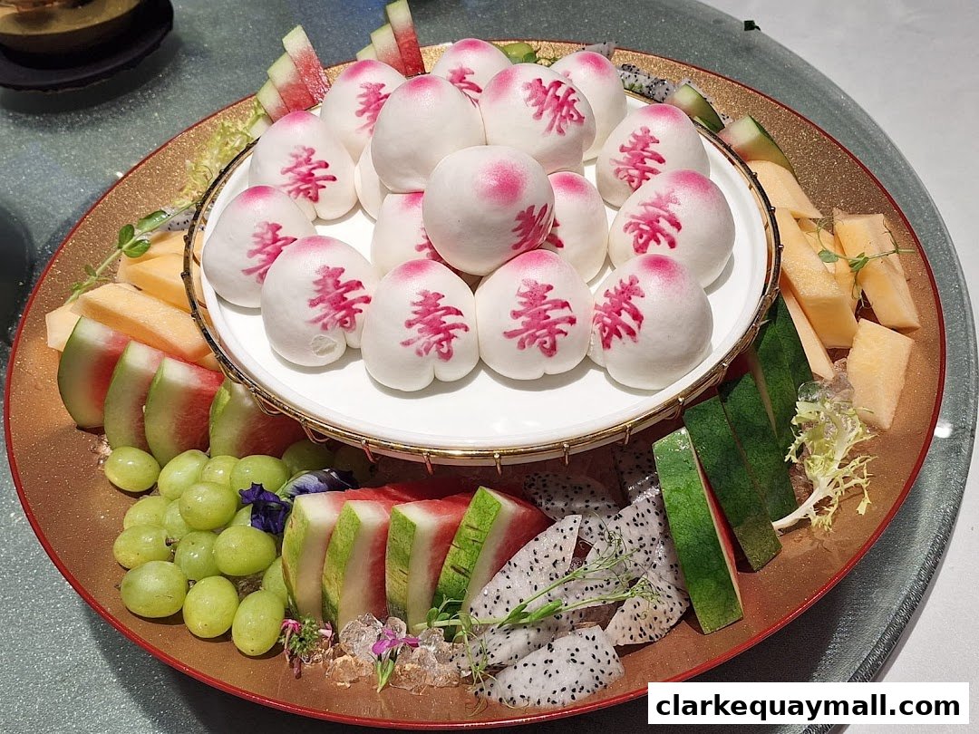 A platter of steamed buns shaped like peaches, surrounded by assorted fresh fruits.