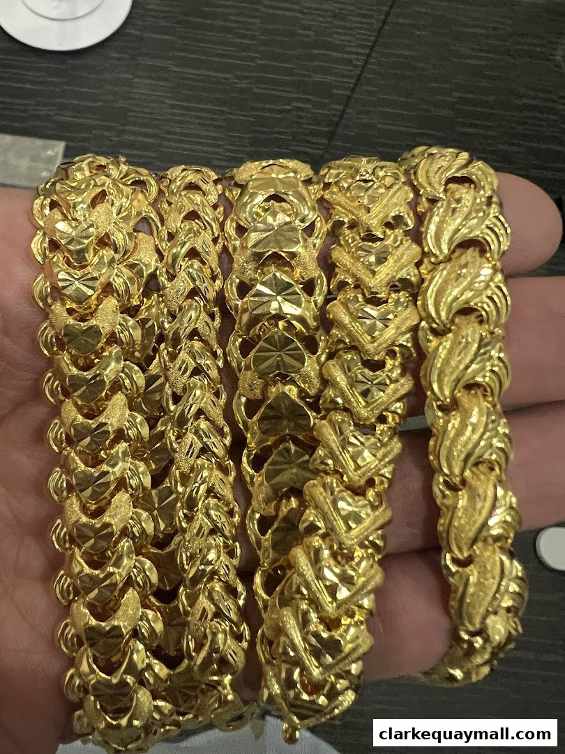 A hand displays several intricate gold bracelets with unique, textured designs.