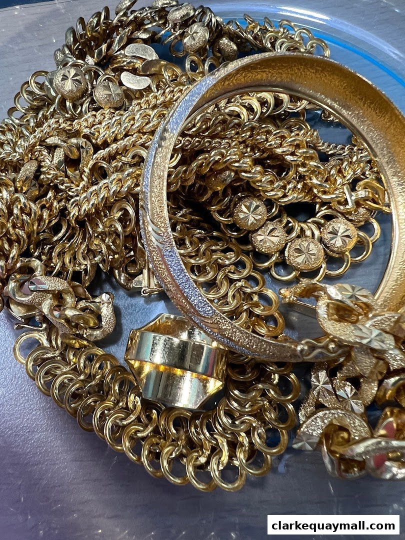 A close-up shot of a pile of assorted gold jewelry, including chains, a bracelet, and a ring.