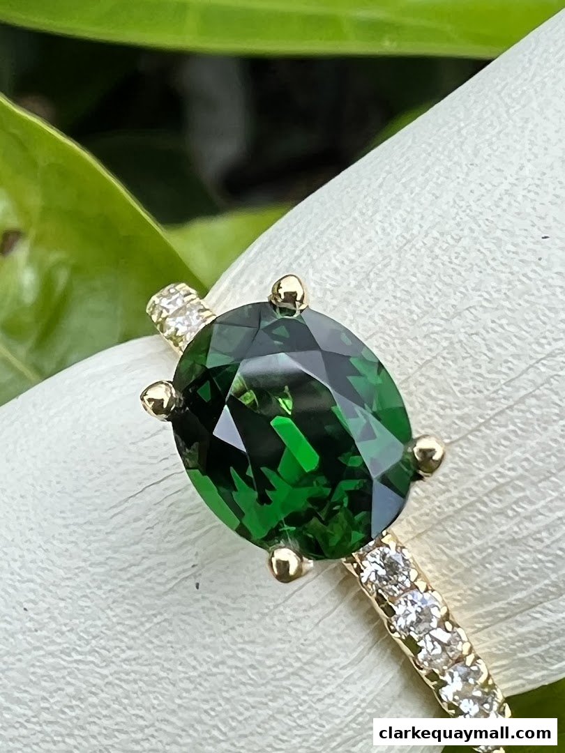 A close-up of an oval-cut green gemstone ring with diamonds on a white surface.