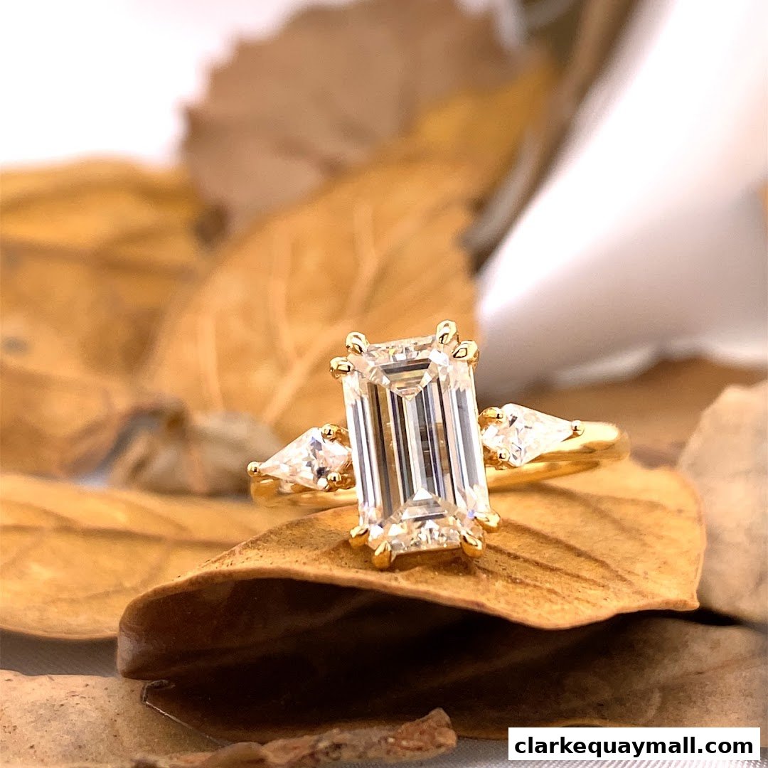 A stunning emerald-cut diamond ring with pear-shaped side stones on a bed of dried leaves.
