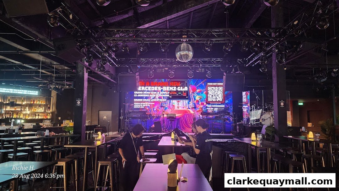 Interior of a bar with a stage, seating, and a large screen displaying event information.
