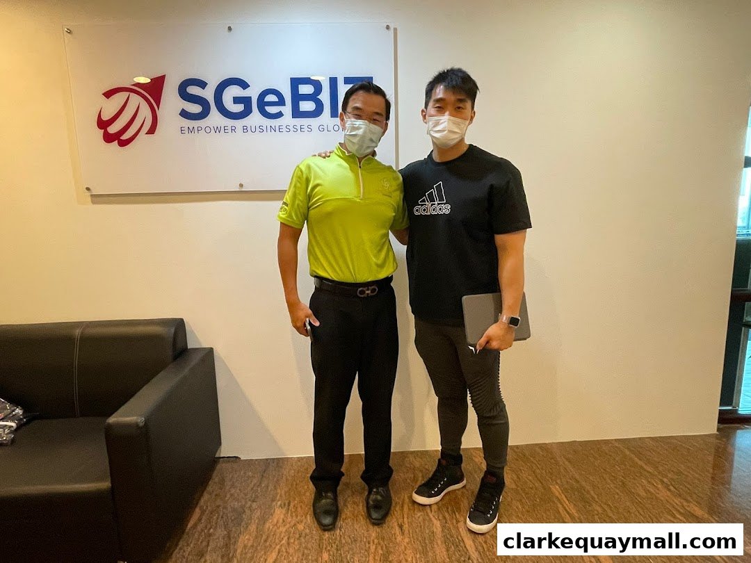 Two men stand in front of the Singapore E-Business Pte. Ltd. logo and a sofa.