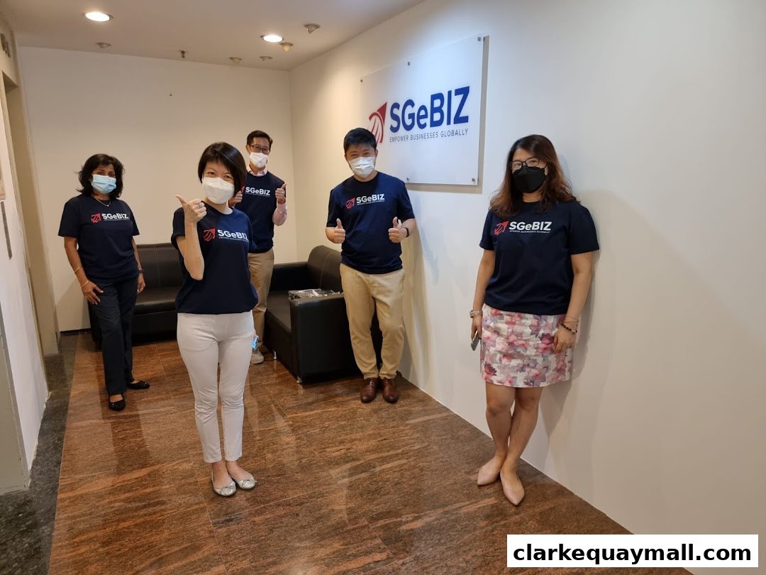 A team of five people wearing SGeBIZ t-shirts stand in an office hallway.