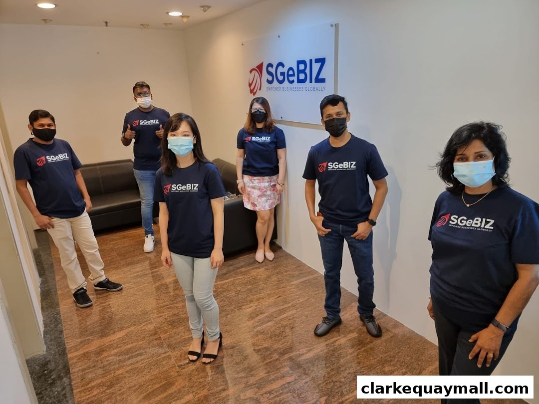 A team of six people wearing matching t-shirts with the SGeBIZ logo stand in an office.
