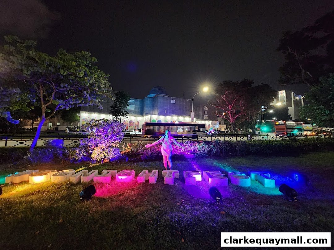 A person stands in front of illuminated letters spelling 'Singapore Festival of Fun' at night.