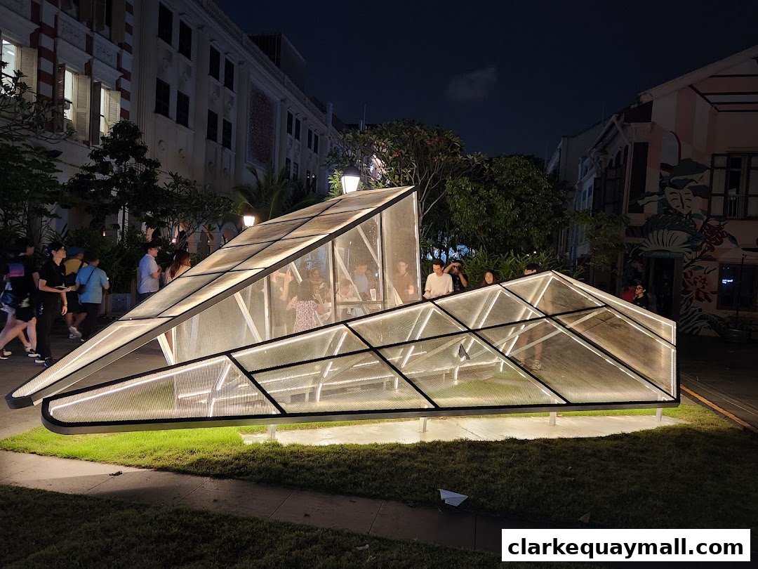 A modern, illuminated structure with people inside, set against a backdrop of buildings at night.