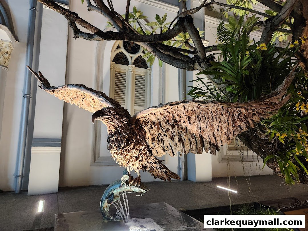 A striking sculpture of an eagle clutching a fish, set against a building with ornate windows and lush greenery.