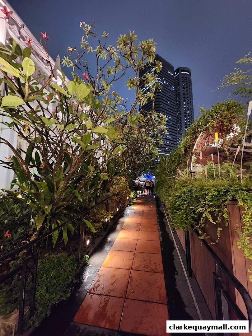 A pathway lined with plants and lights leads towards a building at night.