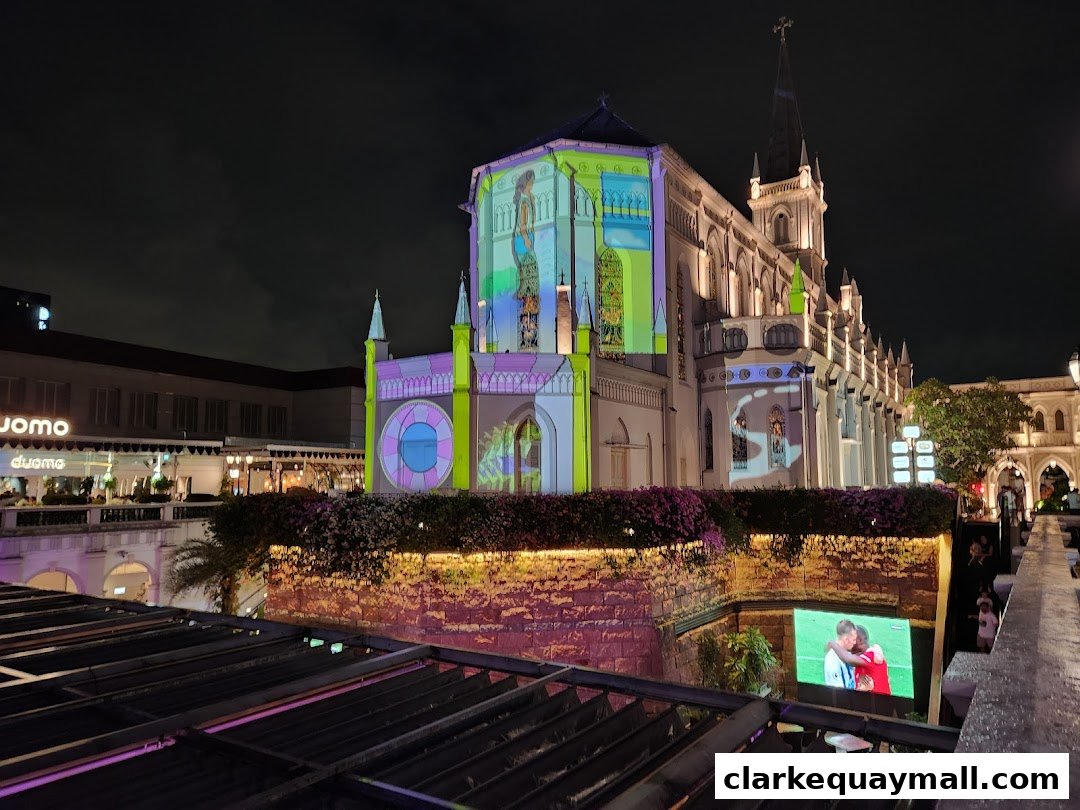 A building illuminated with colorful projections at night, with a screen showing a sports event.