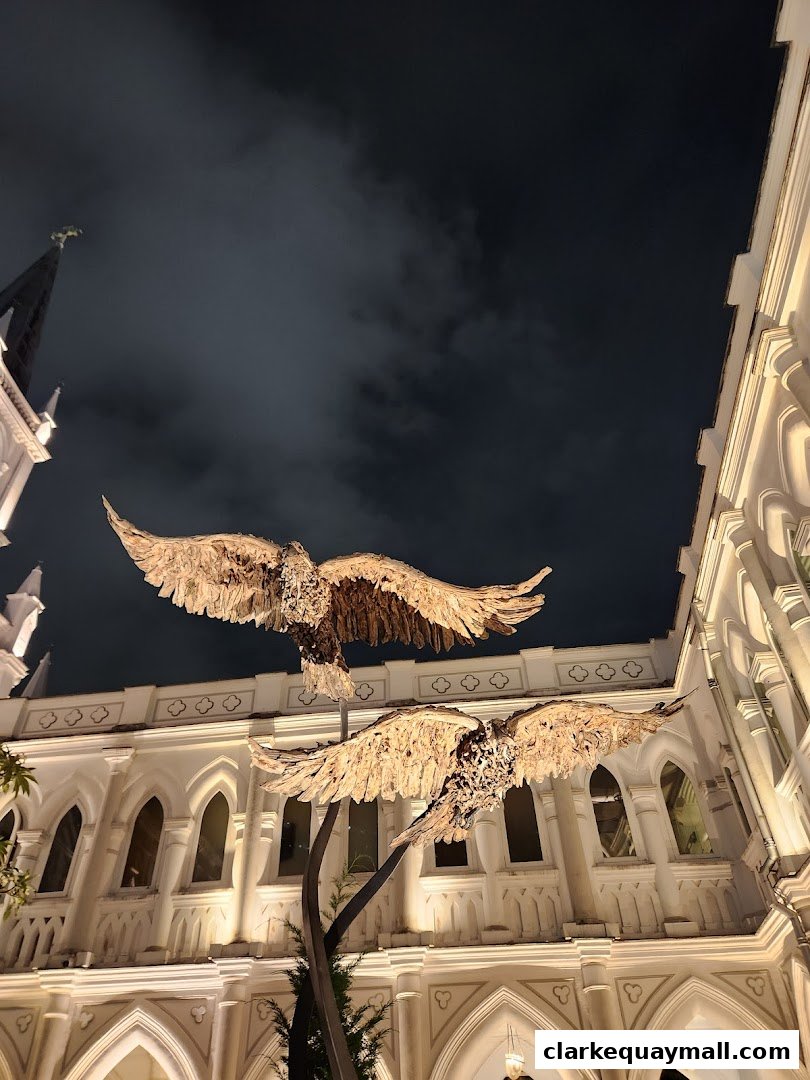 Two large eagle sculptures are displayed in front of a white building with arched windows at night.