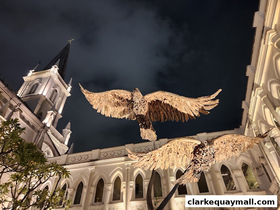 Two large eagle sculptures with spread wings in front of a white building at night.