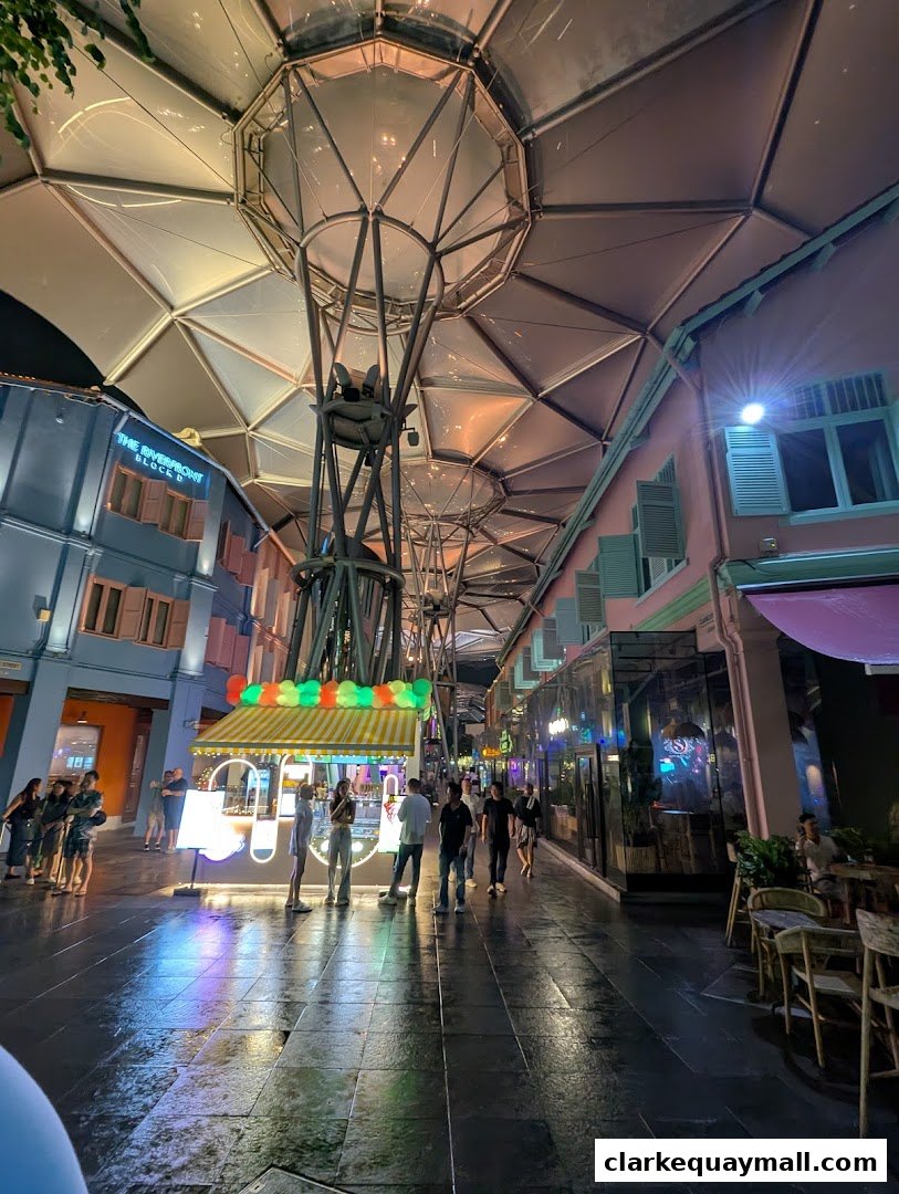 People walk along a covered walkway with shops and outdoor seating at night.