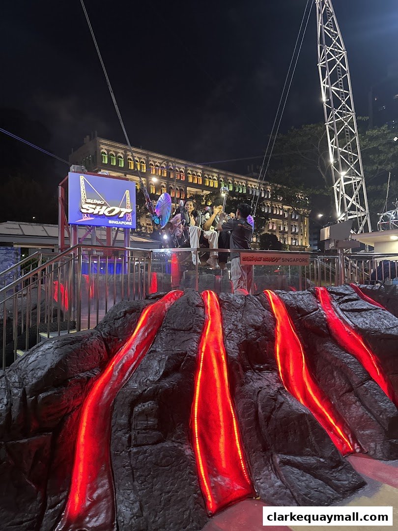 People enjoying the Slingshot Singapore attraction at night with a volcano-themed base.