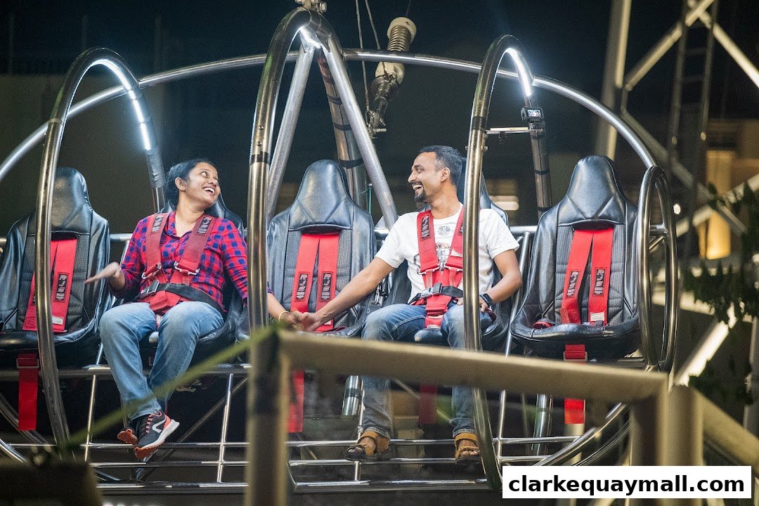Two smiling people in safety harnesses are seated in a ride at night.