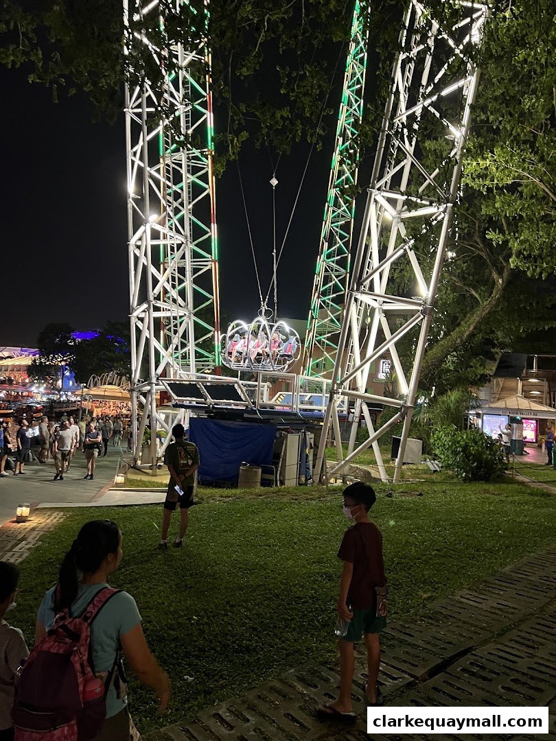People gather at night to experience a thrilling slingshot ride with bright lights.