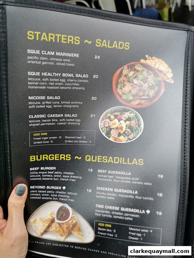 A menu from SQUE Rotisserie & Alehouse featuring starters, salads, burgers, and quesadillas.