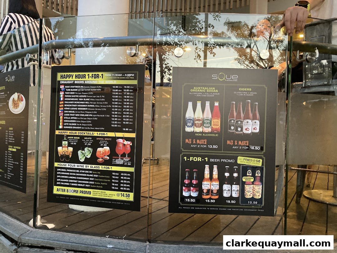 Two menus are displayed on glass, showing happy hour deals and drinks at SQUE Rotisserie & Alehouse.