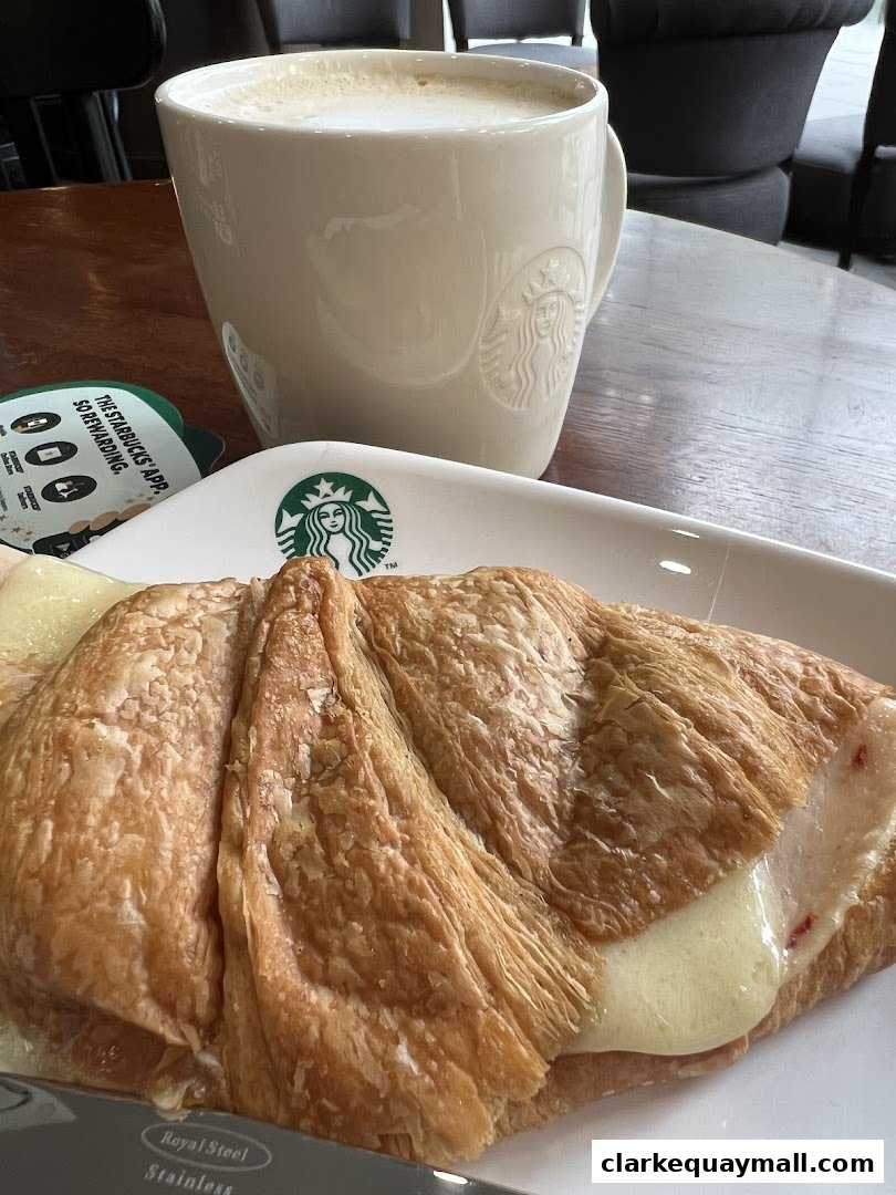 A close-up of a latte and a croissant with melted cheese on a table.
