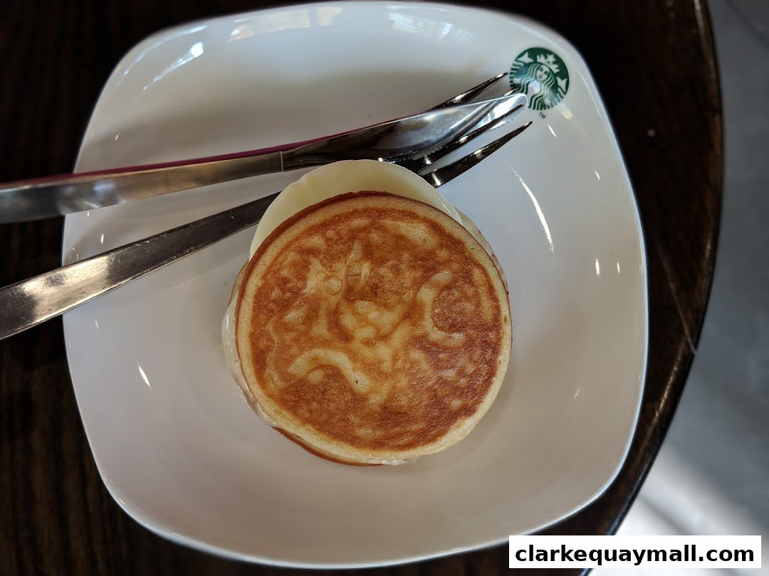 A close-up shot of a Starbucks pancake with cheese and cutlery on a white plate.