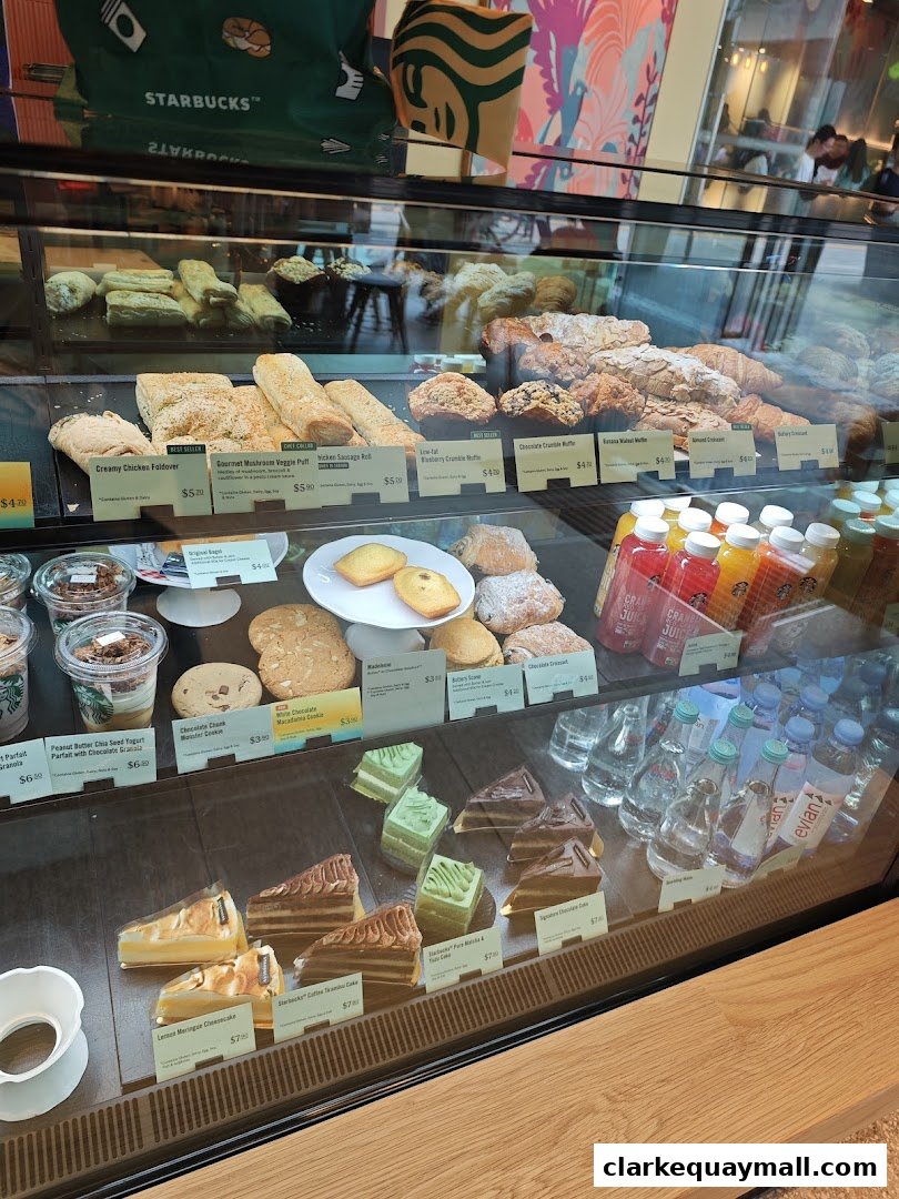 A display case filled with various pastries, cakes, and bottled drinks at Starbucks.