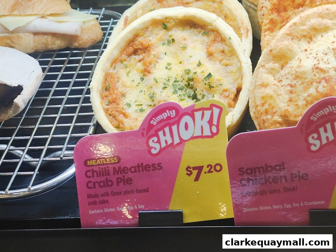 Close-up of savory pies and a sandwich on a cooling rack with price tags.
