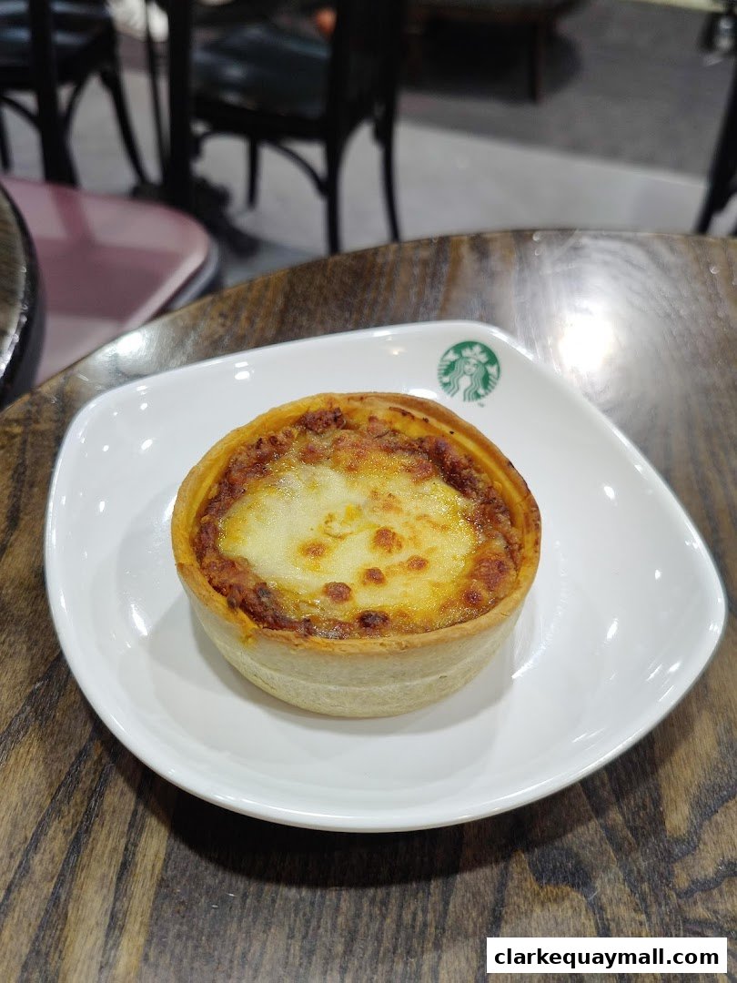 A savory tart with melted cheese on top, served on a white plate with the Starbucks logo.