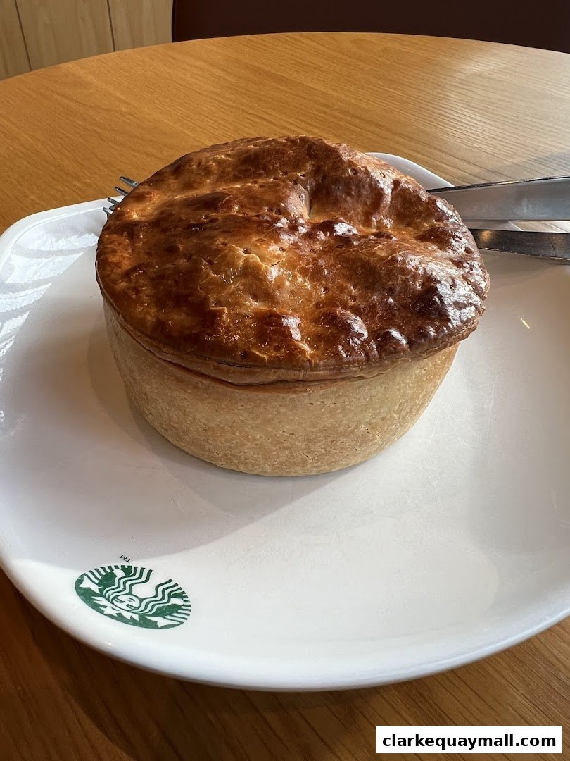 A golden-brown savory pie sits on a white plate with the Starbucks logo.
