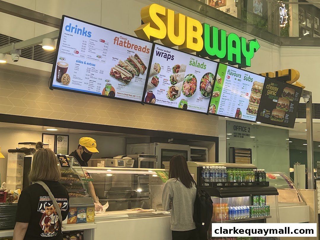 A Subway restaurant menu displayed on digital screens above the counter.