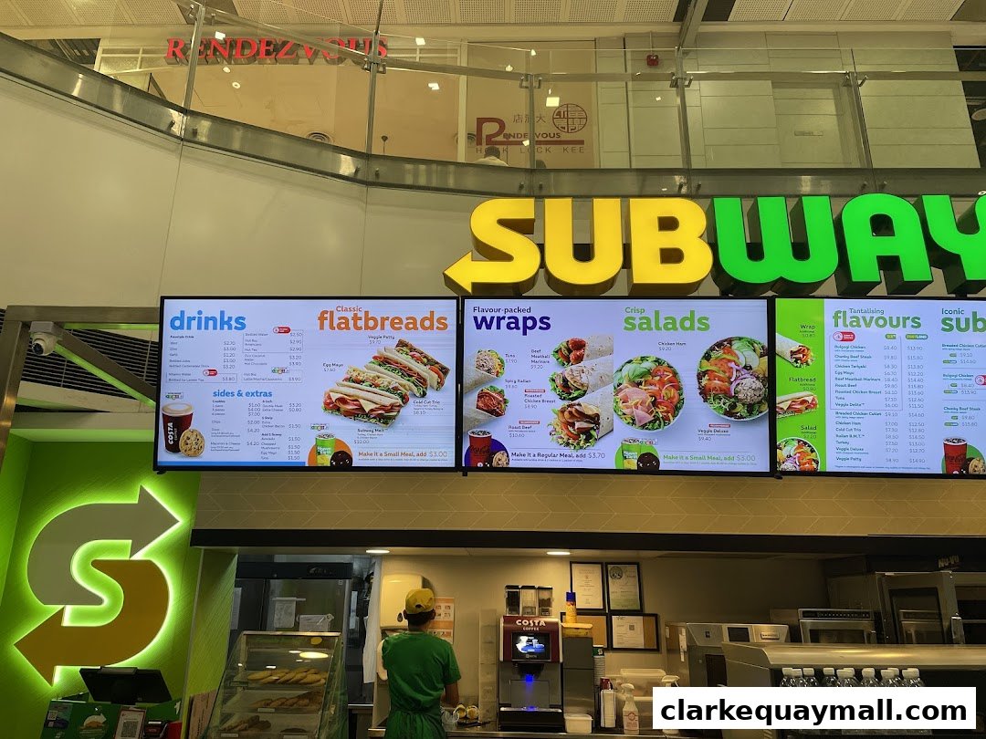 A digital menu board for Subway displaying drinks, flatbreads, wraps, salads, and flavors.
