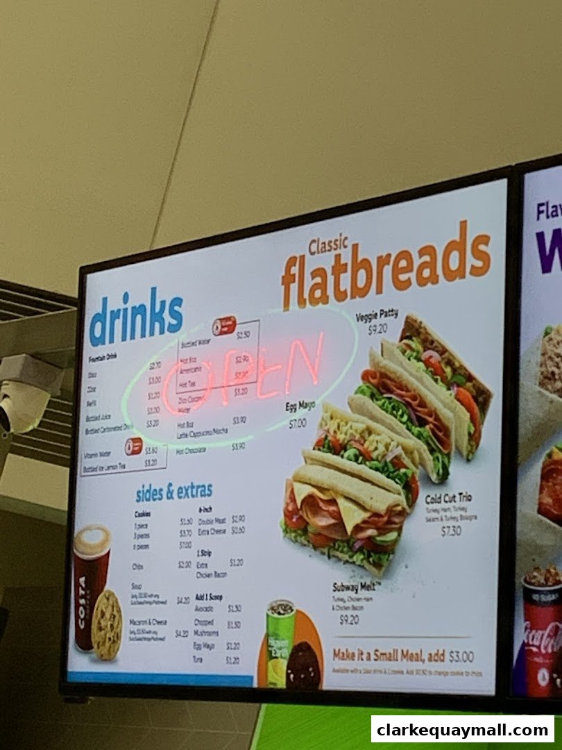 A digital menu board displaying drinks, flatbreads, and sides at a Subway restaurant.