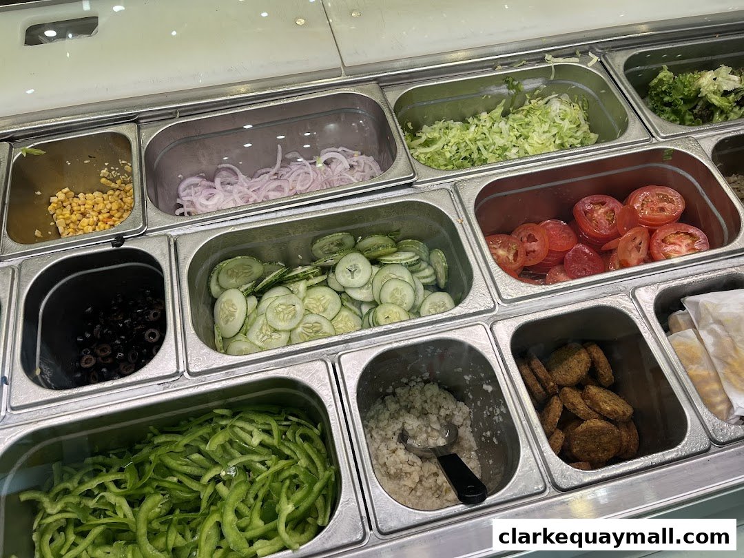 A close-up view of fresh sandwich ingredients displayed in metal containers at Subway.