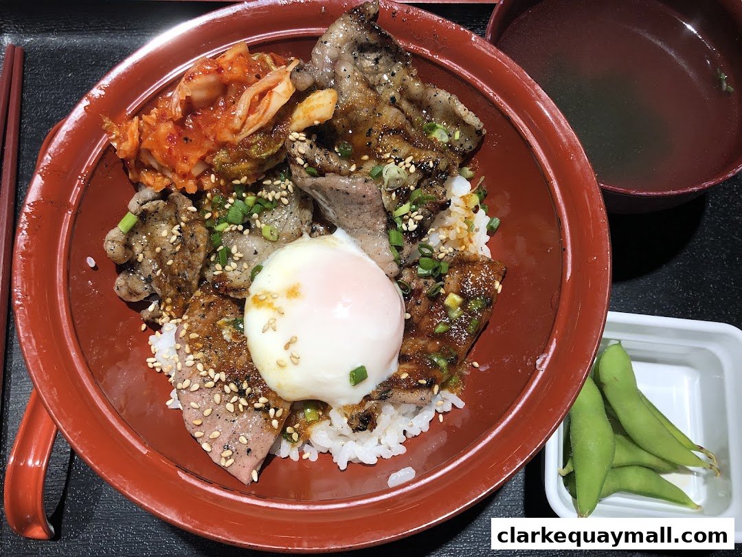 A delicious bowl of rice topped with grilled meat, kimchi, and a soft-boiled egg, served with edamame and soup.
