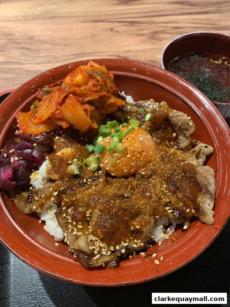 A bowl of rice topped with grilled meat, kimchi, pickled vegetables, and a raw egg yolk.