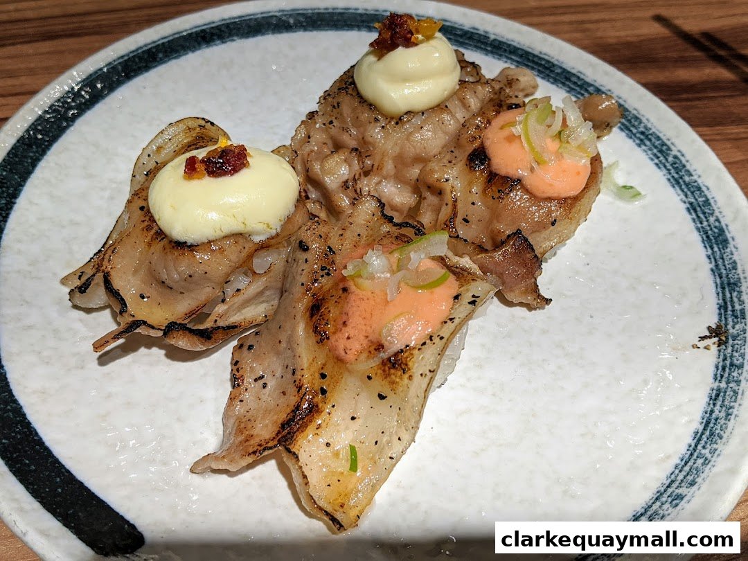 A plate of grilled pork sushi with creamy toppings and scallions.