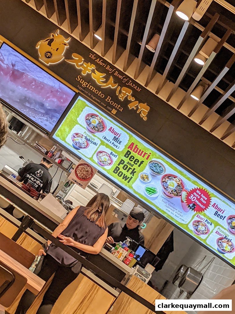 A customer orders at a counter with a large menu board displaying various beef bowls.