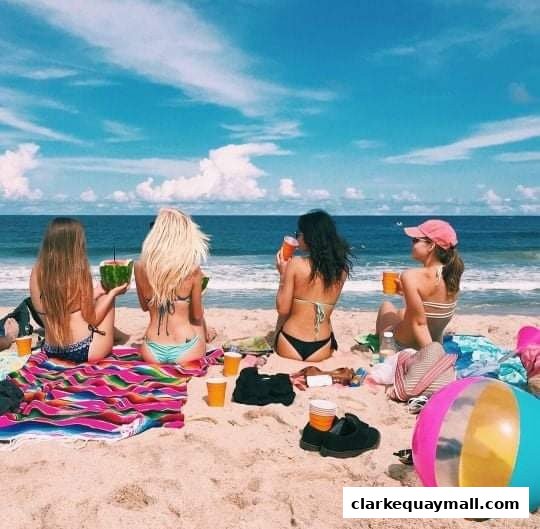 Four friends enjoy drinks and watermelon on a sunny beach day.