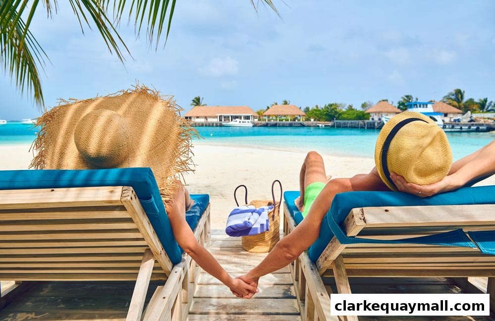 Couple relaxing on beach chairs by the turquoise ocean with tropical resort in background.