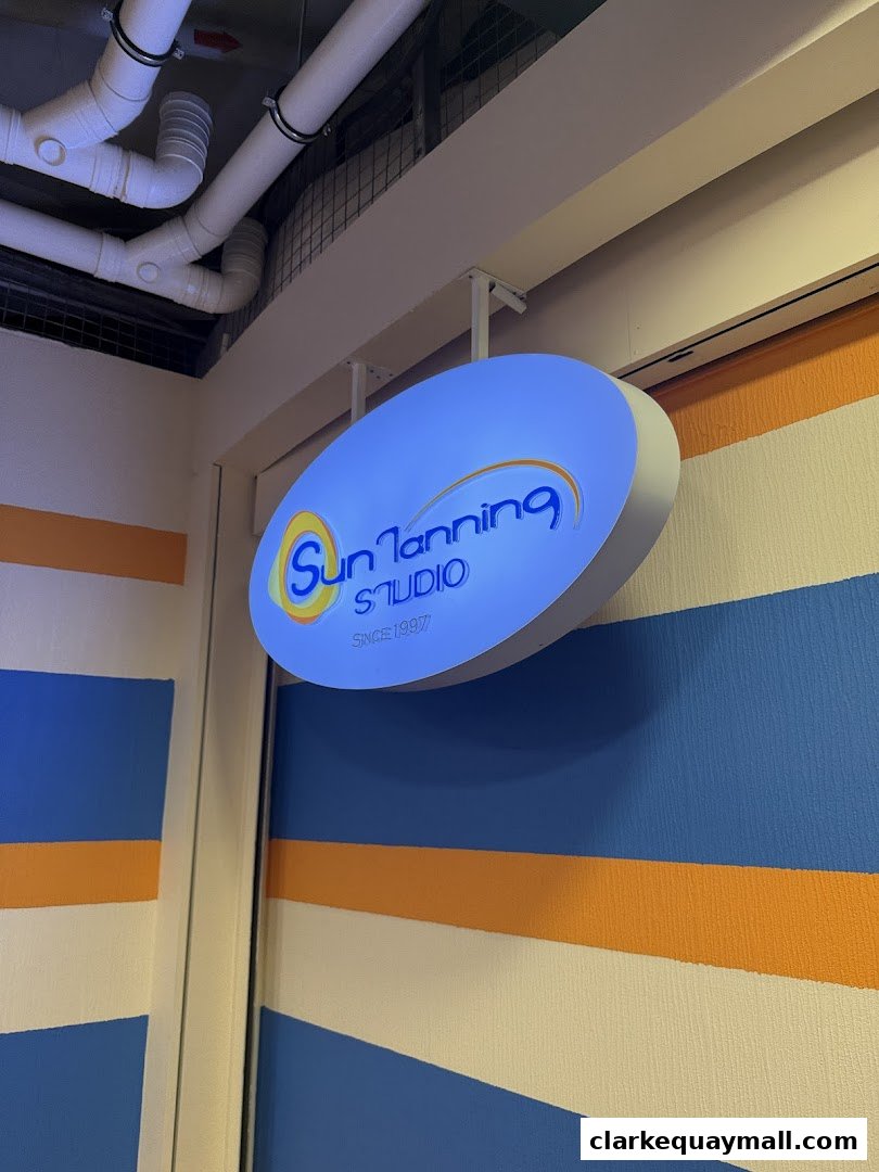 A glowing oval sign for Sun Tanning Studio hangs on a wall with colorful stripes.