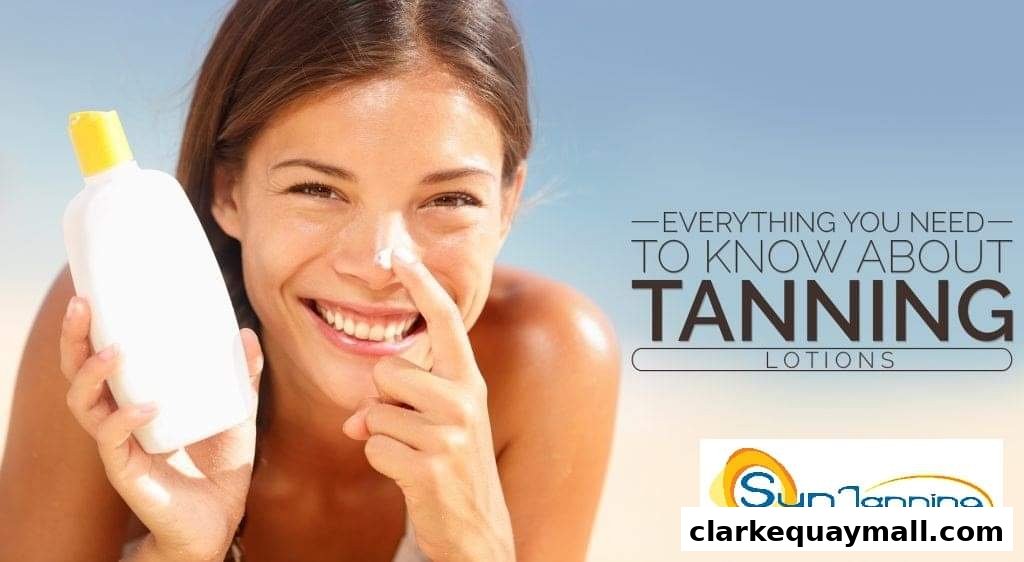 A smiling woman applies tanning lotion to her nose with a bottle in her hand.