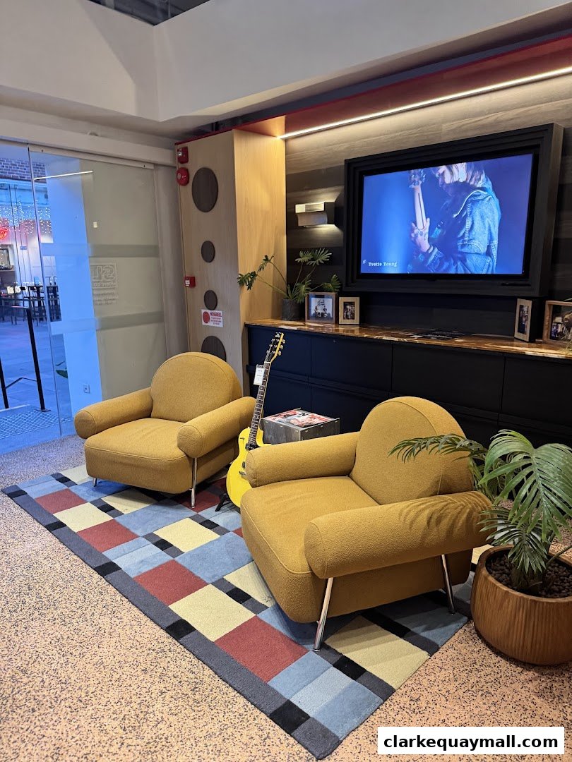 A cozy seating area with two mustard chairs, a guitar, and a TV displaying a music video.